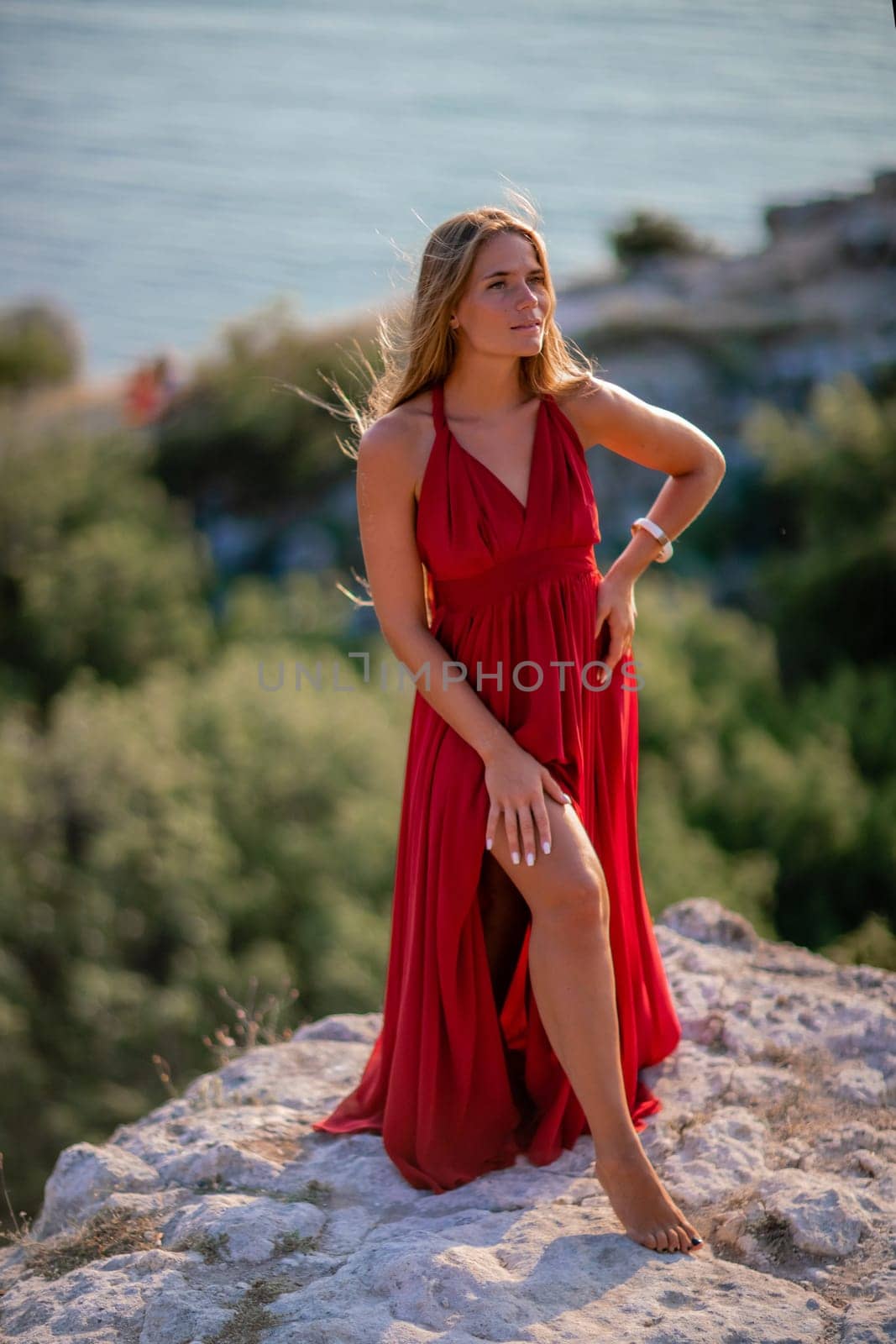 Woman sunset sea red dress, back view a happy beautiful sensual woman in a red long dress posing on a rock high above the sea on sunset