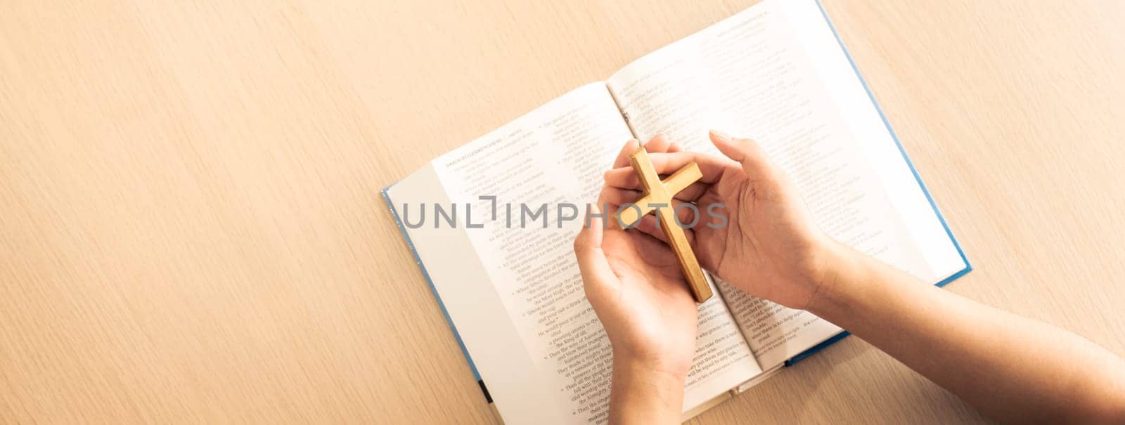 Female god believer holding wooden cross on opened holy bible book at light wooden church table. Top view. Concept of hope, religion, faith, christianity and god blessing. Warm background. Burgeoning.