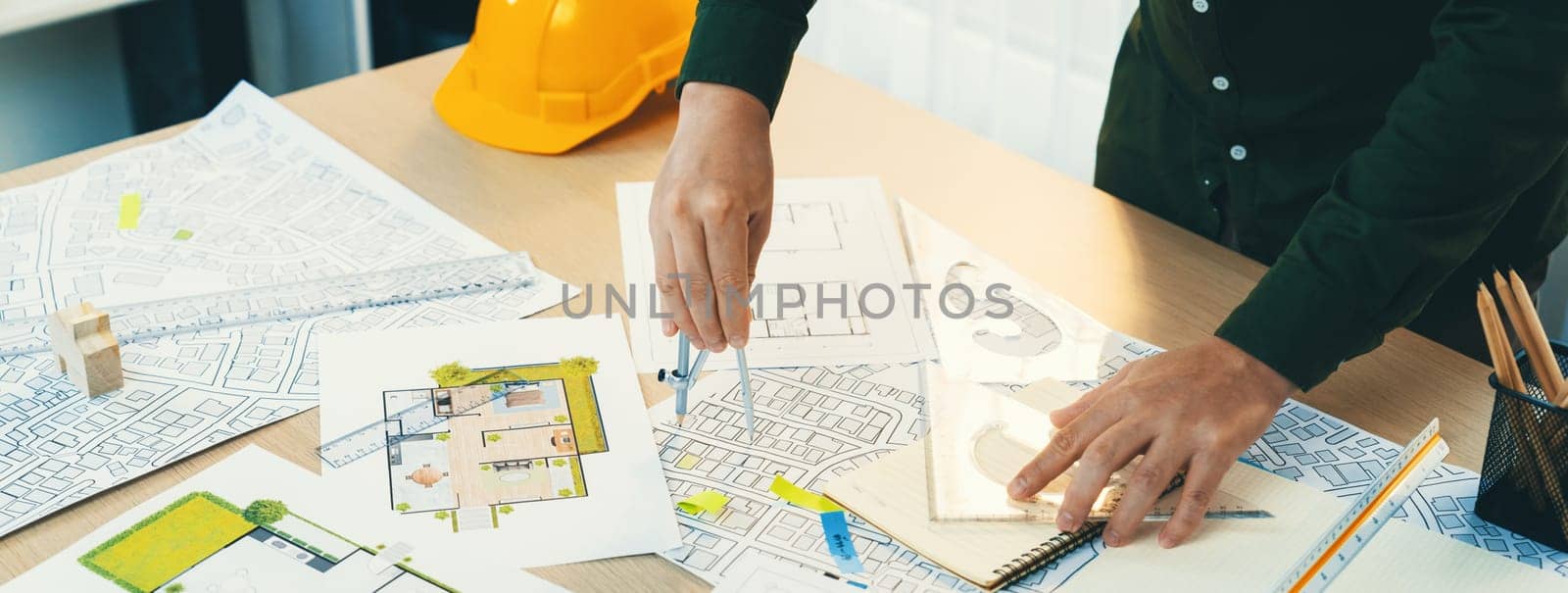 A portrait of architect using divider to measure blueprint. Architect designing house construction on a table at studio, with architectural equipment scattered around. Focus on hand. Delineation