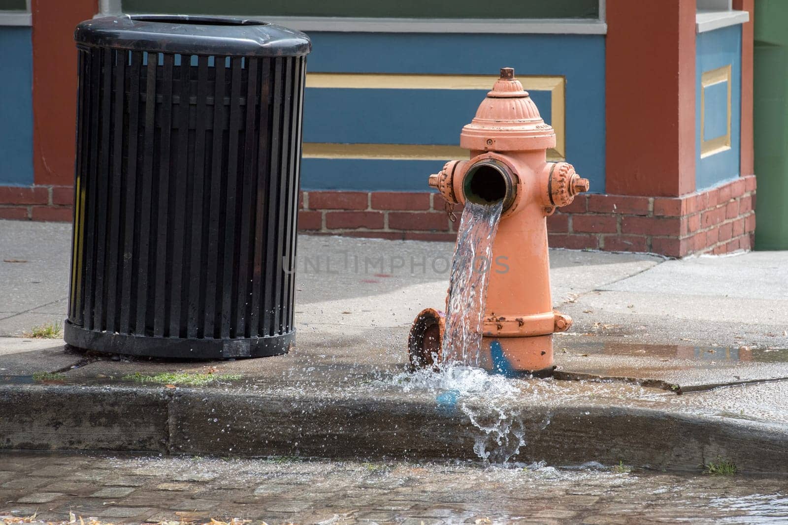 Street orange hydrant spreading water on the street by AndreaIzzotti