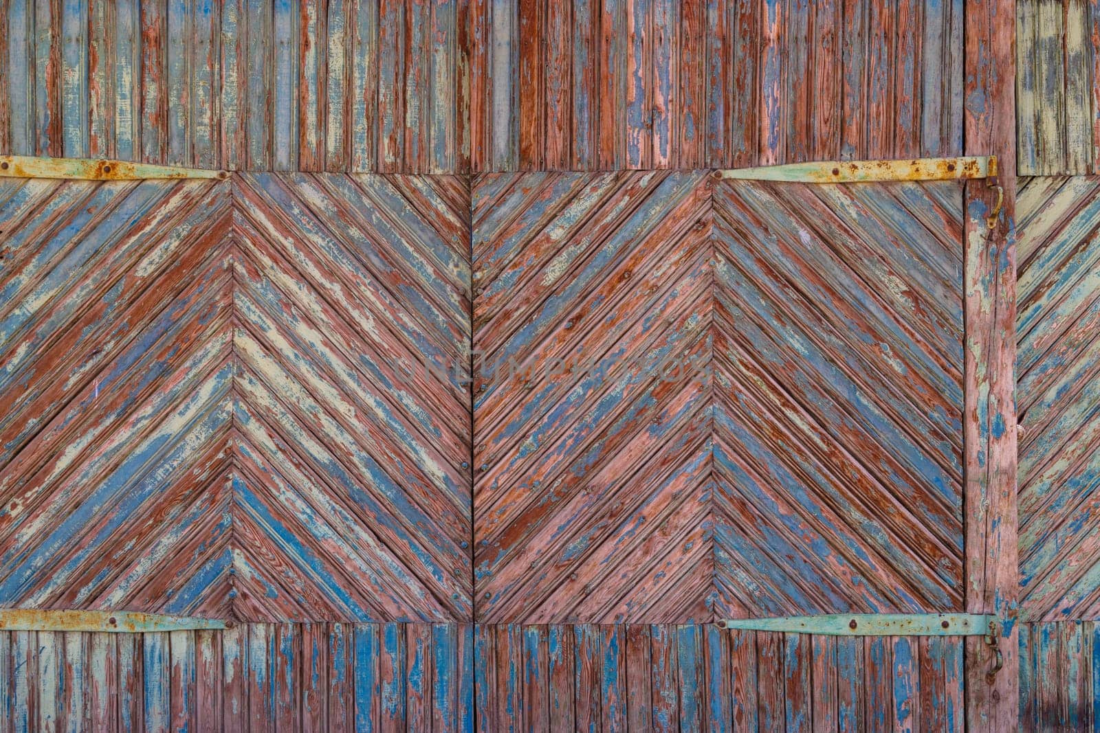Artistic old wooden planks gate texture with peeled brown and blue paint layers under sun-bleached blue paint layer. Full-frame flat background and texture.