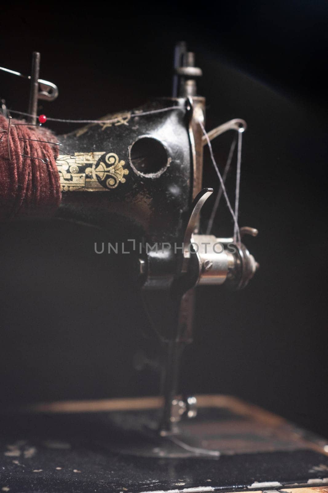 An old sewing machine stands on the table at home ready to work and sew. Classic retro style manual sewing machine ready for sewing work. The machine is old style made of metal with floral patterns