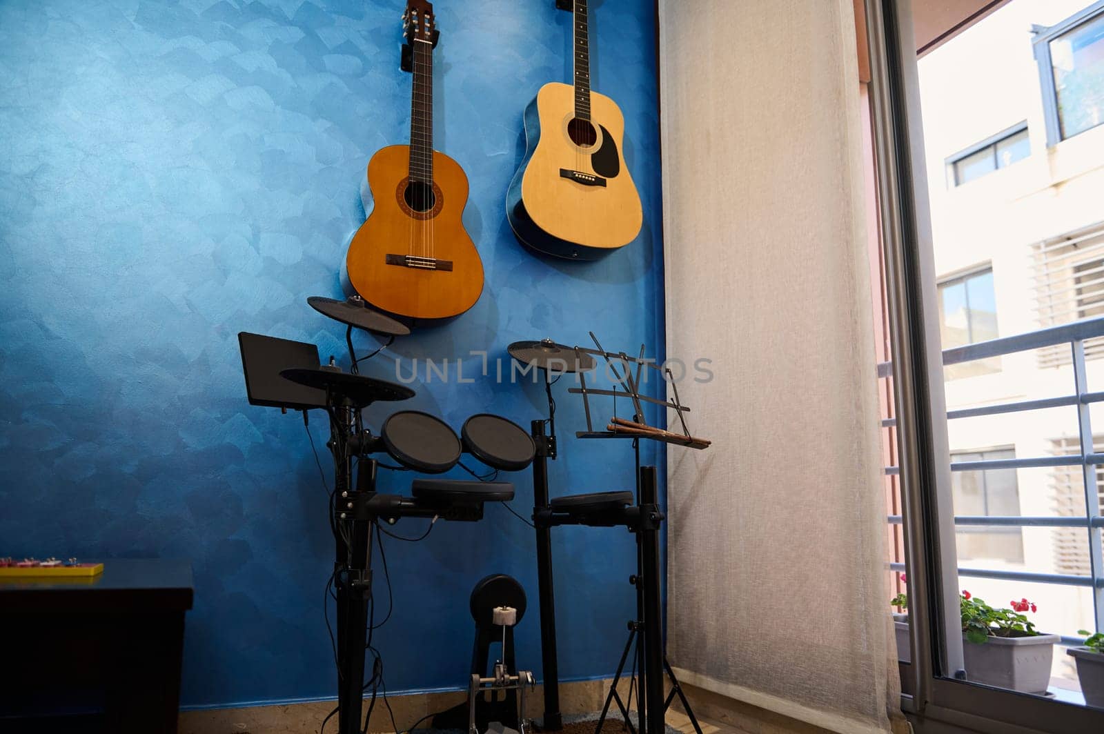 A modern interior of a music studio at home. Acoustic and electric guitars hanging on blue color wall and drum set. Hobbies and leisure. Musician's room for playing and learning music. Horizontal shot