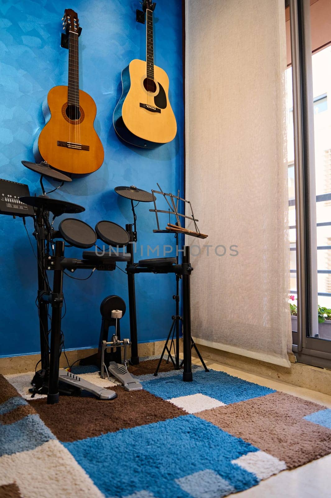 Modern interior of a music studio for home use. Acoustic nd electric guitars hanging on blue color wall and drum set. Hobbies and leisure. Musician's room for playing and learning music. Vertical shot