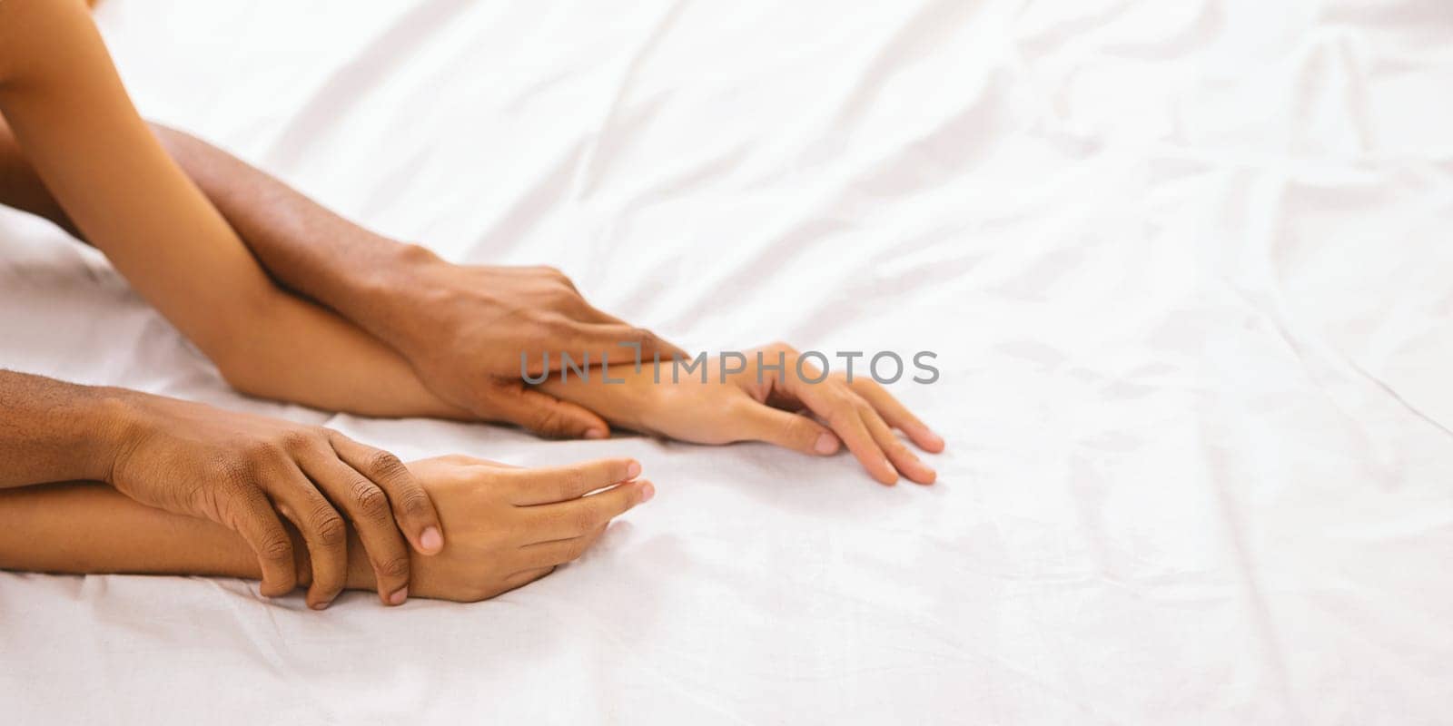 African American couple's hands express closeness as they lay in bed, with a focus on the bond they share above white linens