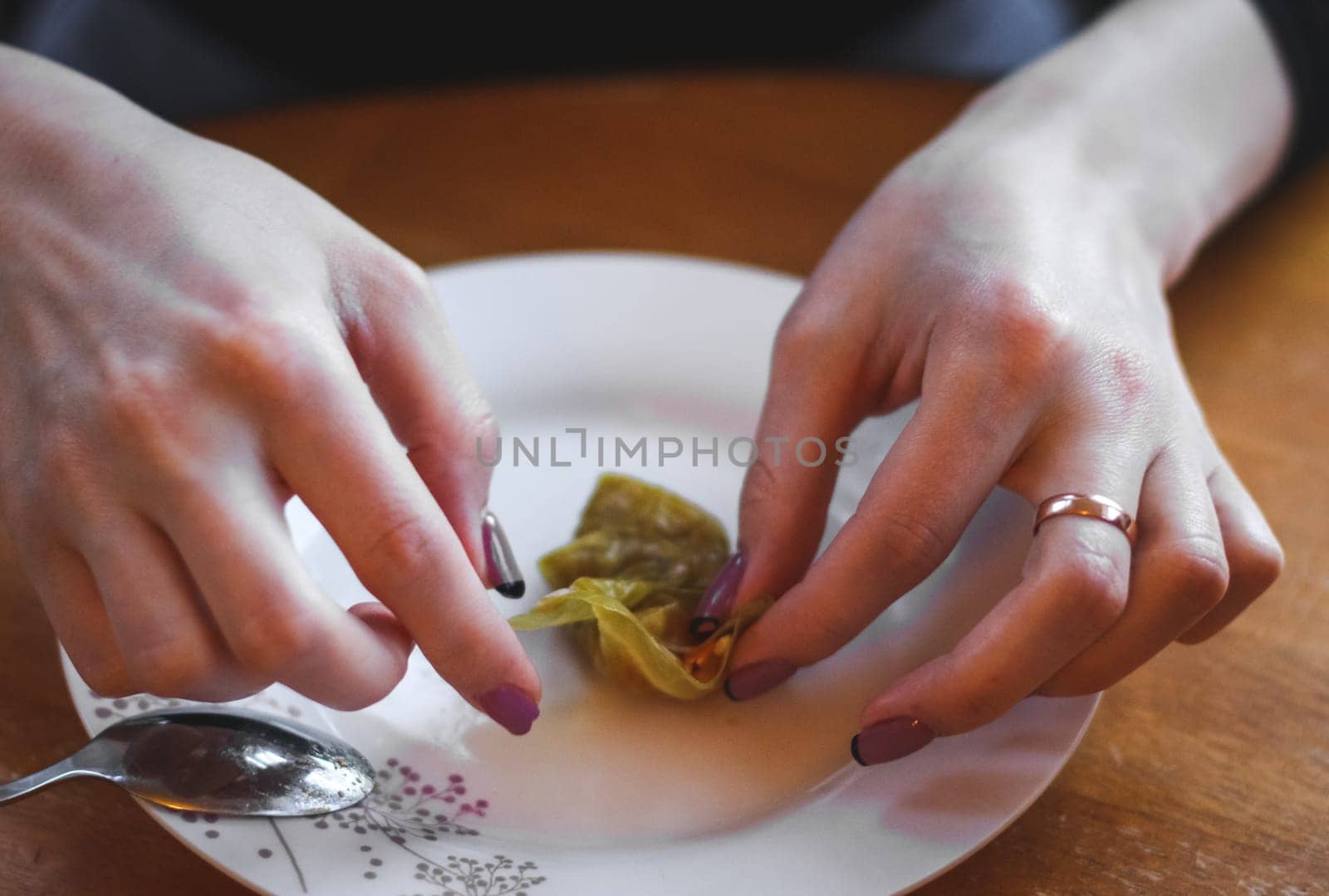 The hands of a young woman roll up a raw sauerkraut leaf with meat and rice filling in a plate while sitting at a round table in a flat kitchen. The concept of step by step instructions, home cooking, traditional recipes, national cuisine, cabbage rolls, dolma.