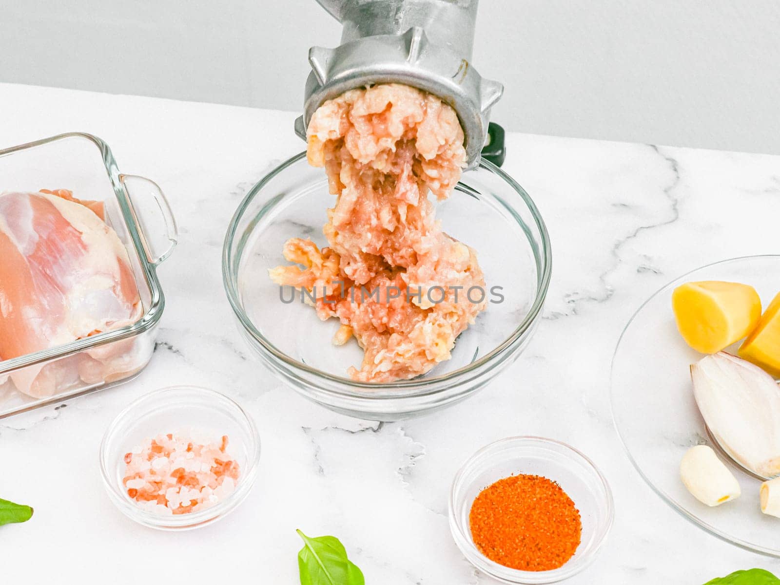 Hand drawn retro mince with minced meat,glass dish,boneless chicken thighs,pink salt,peeled onions,garlic,peeled potatoes in saucer and basil leaves on marble table,closeup side view.Concept of homemade minced meat and healthy eating.