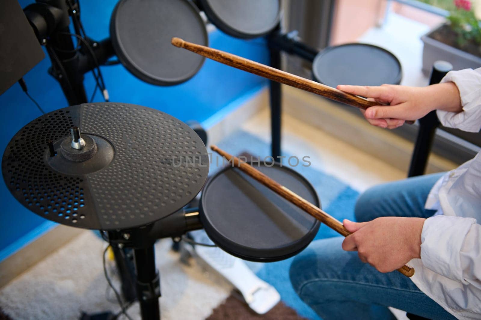 Close up view from above of teenage drummer hands. Teen boy playing drums in music studio. Top view of boy musician beating on the black cymbals with drumsticks, performing sound playing on drum set