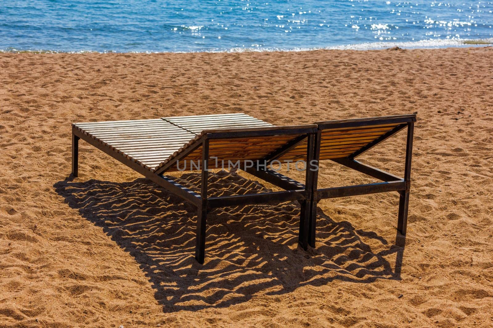 empty outdoor lounge chairs on sandy beach near blue water. by z1b