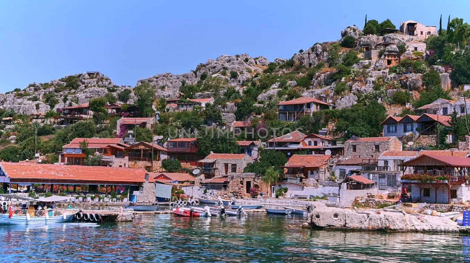 Charming Mediterranean village on Turkish coast with red-roofed houses, historic stone castle, and stunning sea views, perched on cliffs overlooking the azure waters of the Mediterranean Sea.