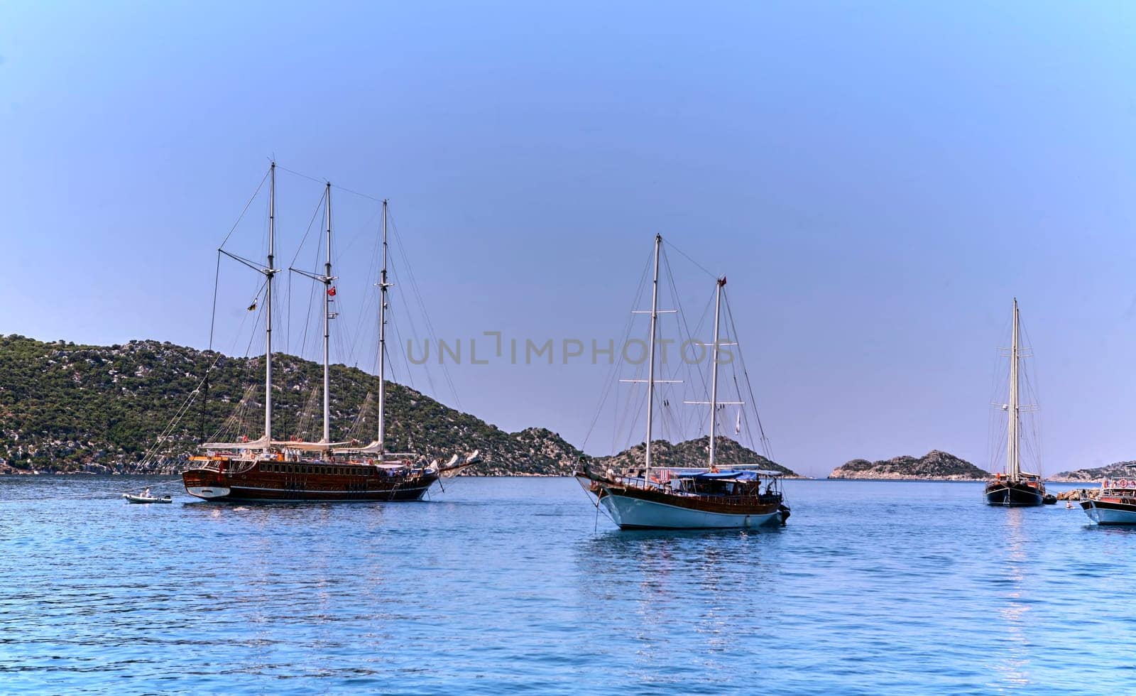 Wooden sailing boat anchored in a calm sea with mountains in the background by Hil