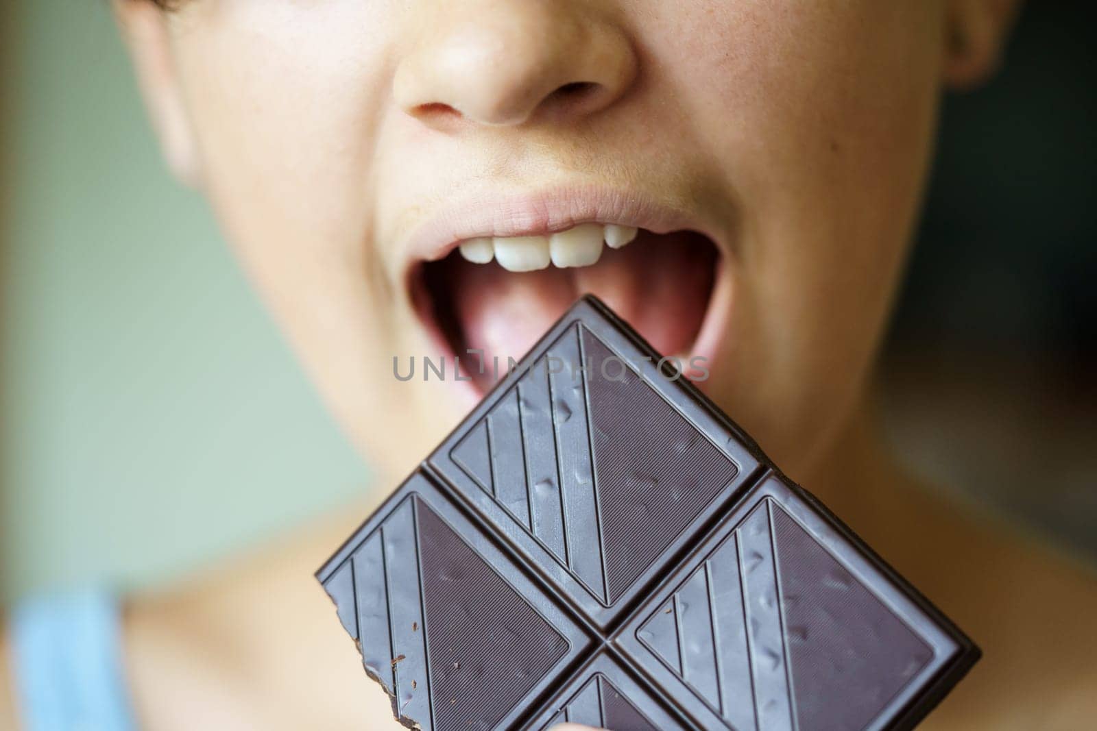 Closeup of crop anonymous teenage girl with mouth wide open about to eat chocolate bar at home