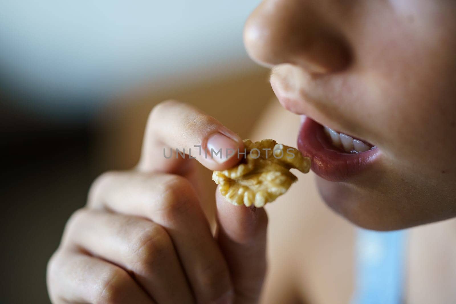From above closeup of crop anonymous teenage girl eating healthy walnut kernel at home