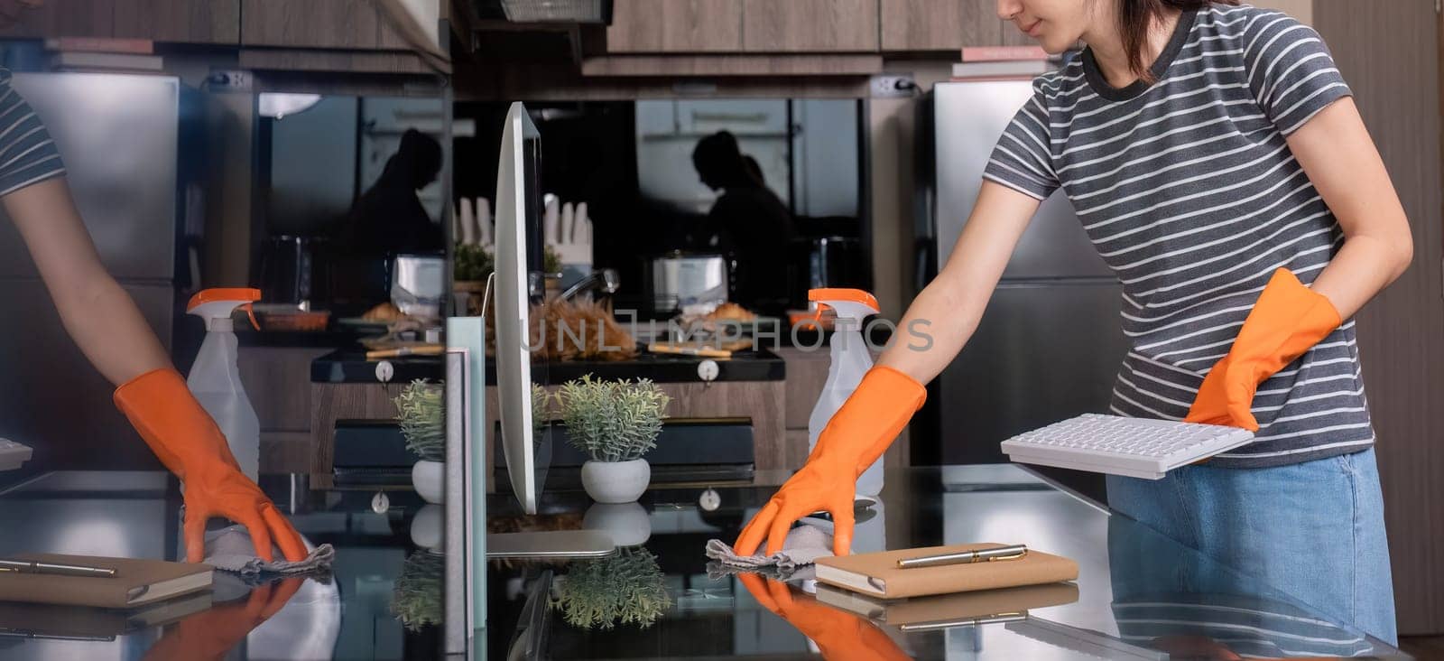 Beautiful young housewife wearing orange housekeeping gloves uses spray and cloth to clean the table in the living room..