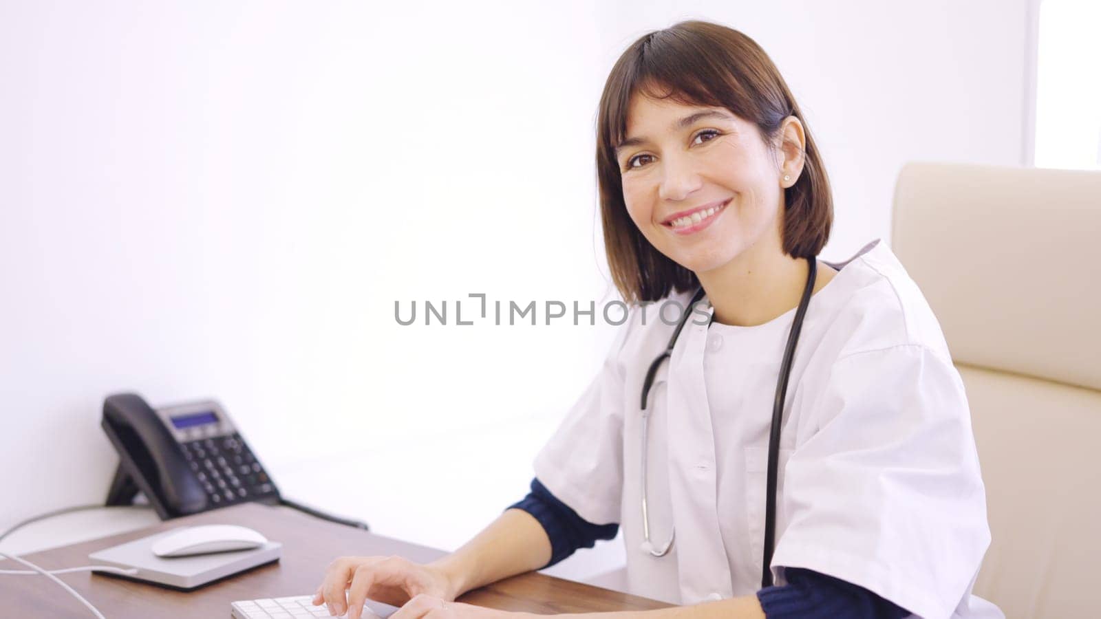 Female doctor using computer and smiling at camera in a clinic