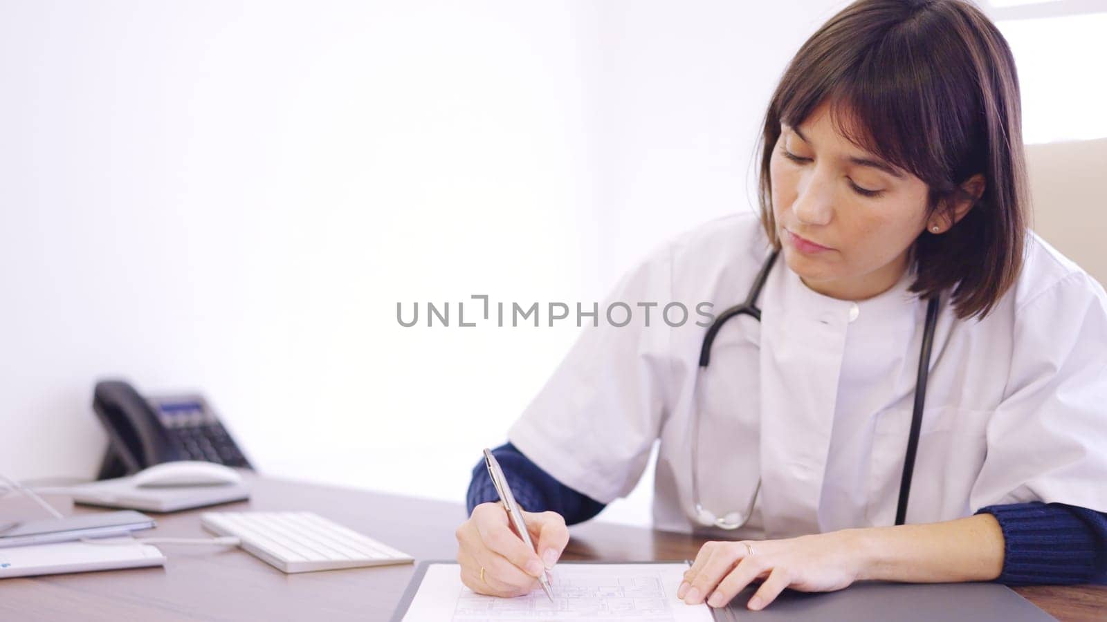 Female doctor filling a report sitting on a clinic by ivanmoreno