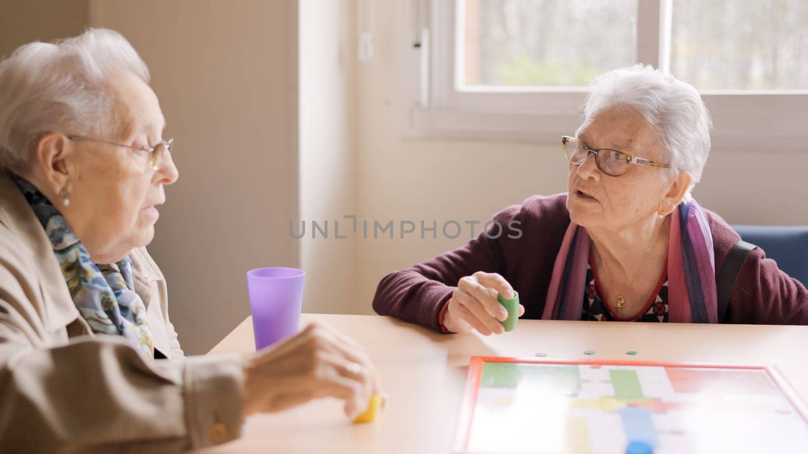 Two old friends having fun playing Parcheesi board game in a geriatric