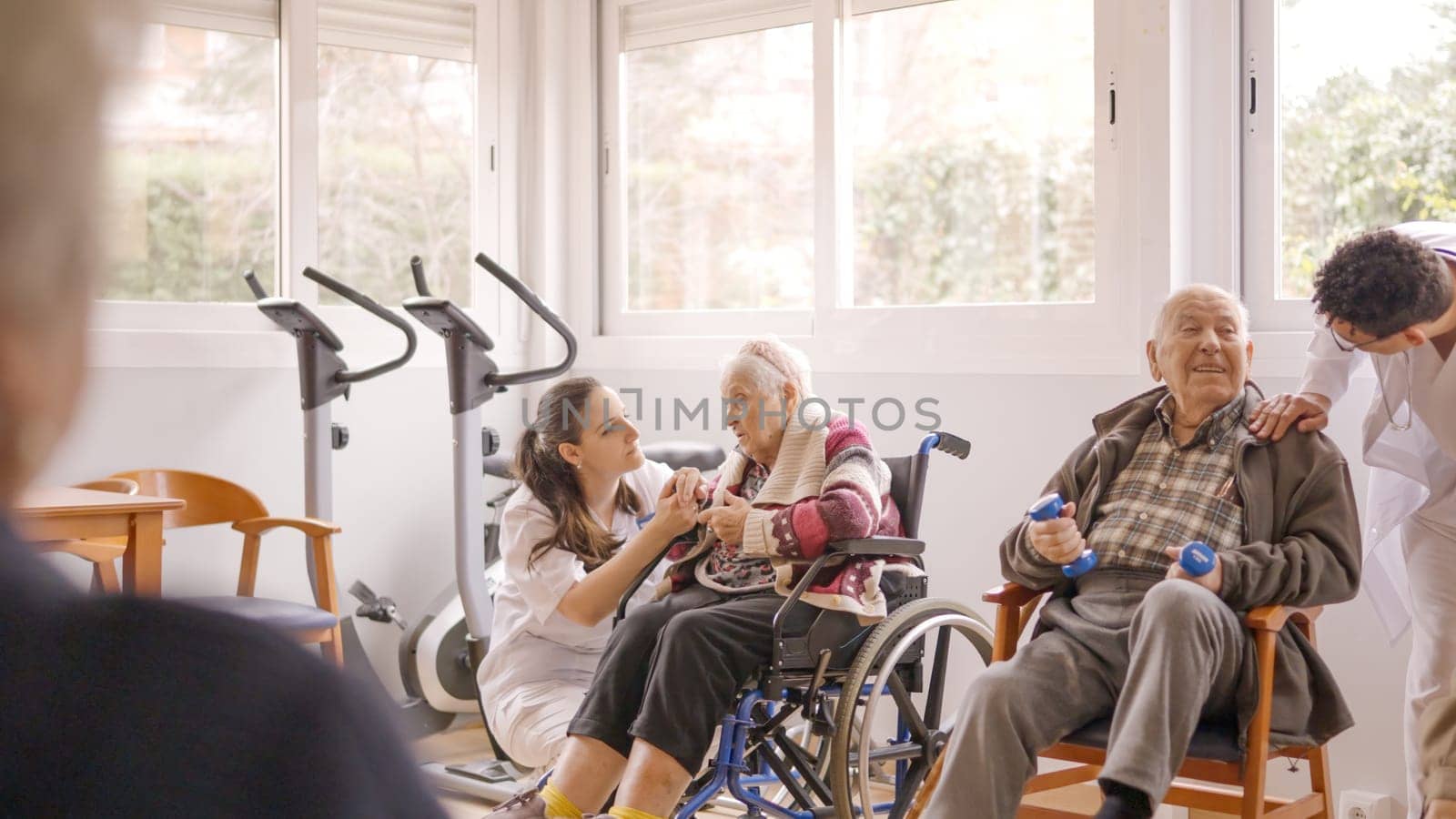 Physiotherapists talking to senior people while exercising in geriatrics by ivanmoreno