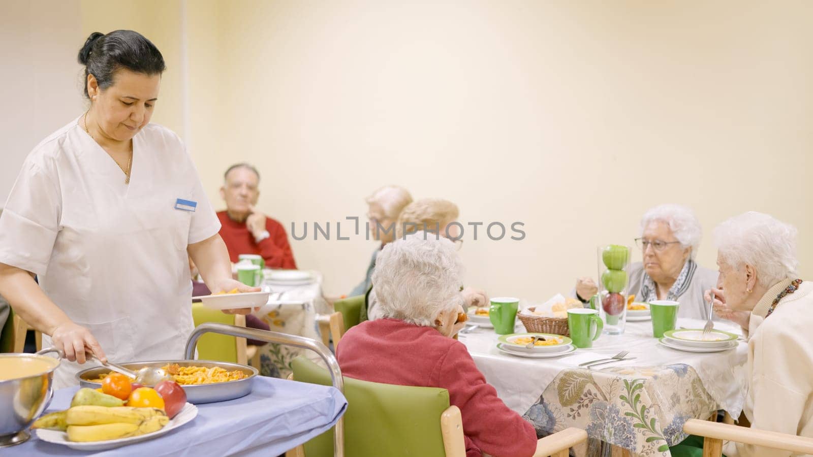 Female cook serving food to a group of seniors in a geriatric