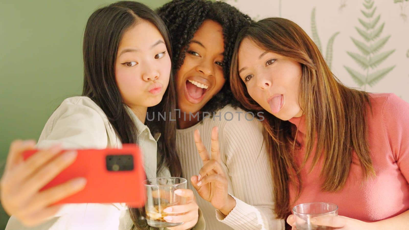 Group of multiracial women pulling funny faces while taking a selfie sitting on the sofa at home
