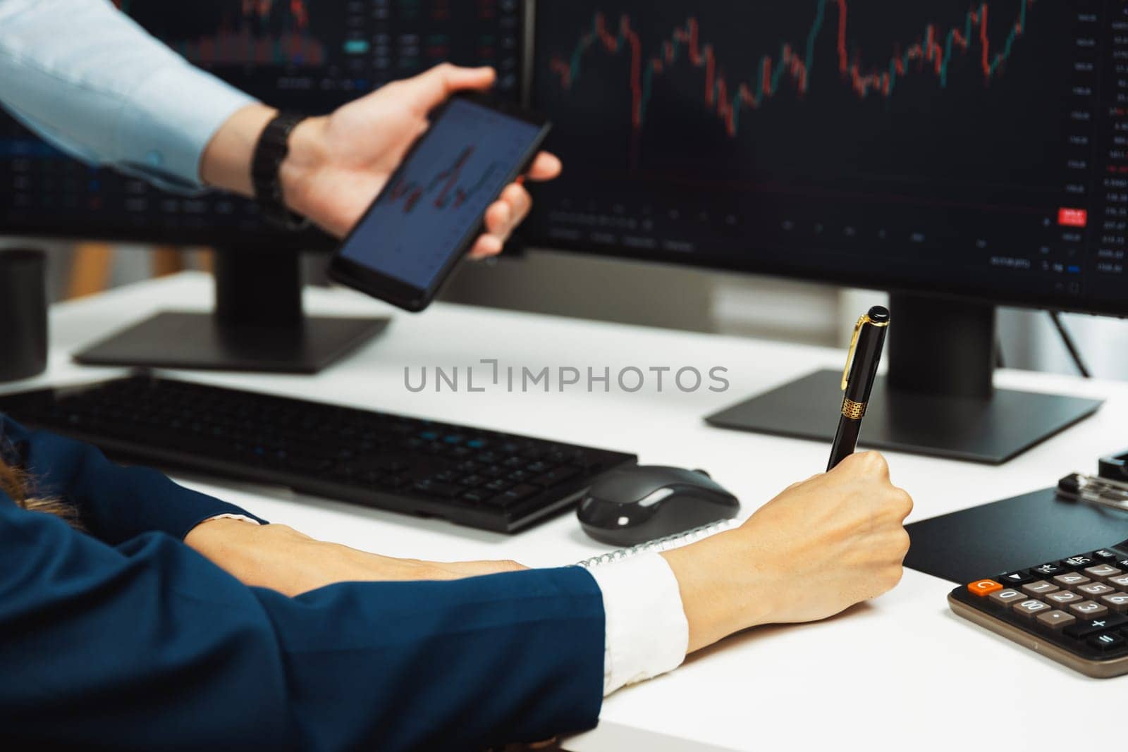 Cropped pointing hand with pen in businessman, checking with holding smartphone by woman investor online website program application with dynamic stock market at home office at back side. Infobahn.