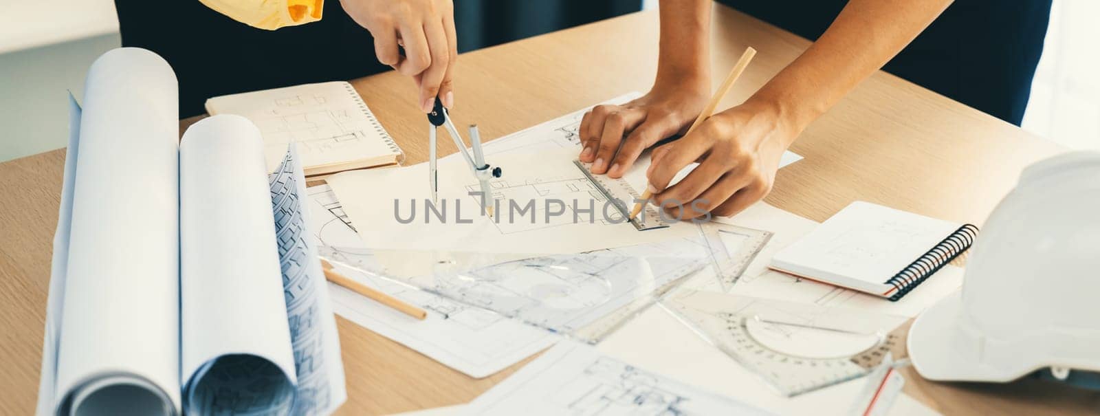 Professional architect team used divider measure during draft blueprint on table with architectural document, safety helmet and blueprint scatter around. Closeup. Focus on hand. Delineation.