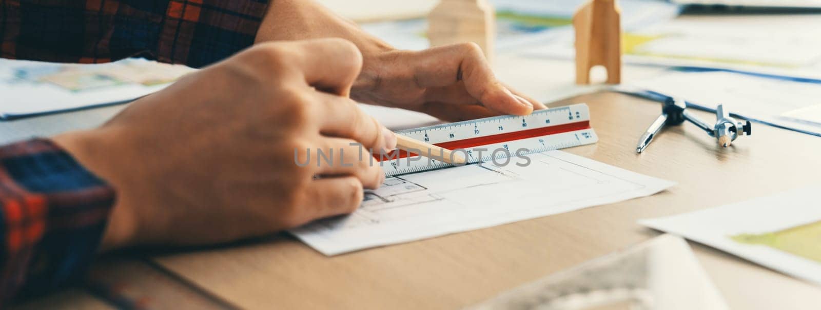 Closeup of architect engineer hand using ruler to mature and draw a blueprint on meeting table with wooden block, pencil and blueprint scatter around at architectural modern office. Delineation.