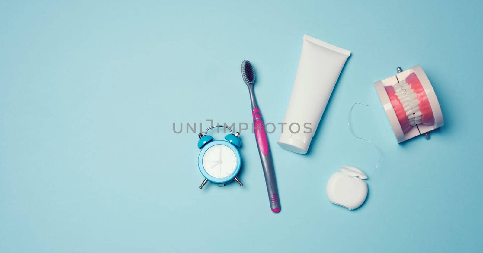 Model of a human jaw with white teeth, dental floss and toothpaste on a blue background, top view	