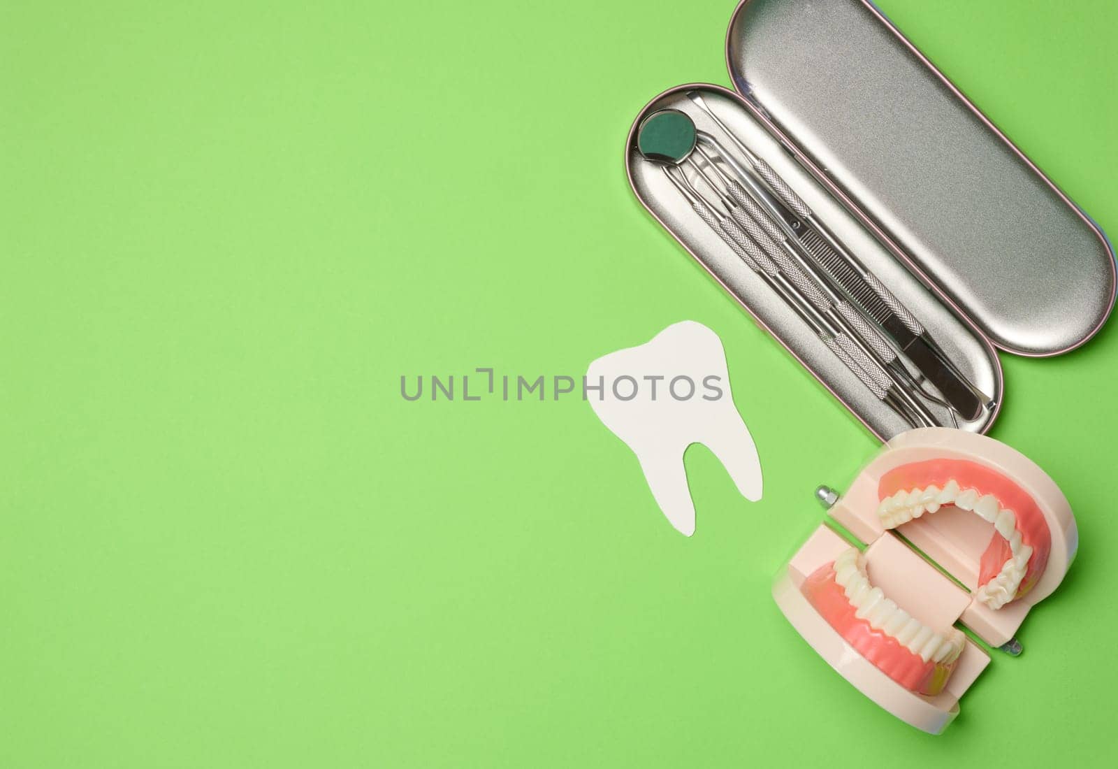Metal dentist tools, plastic jaw model with white teeth on a green background, top view