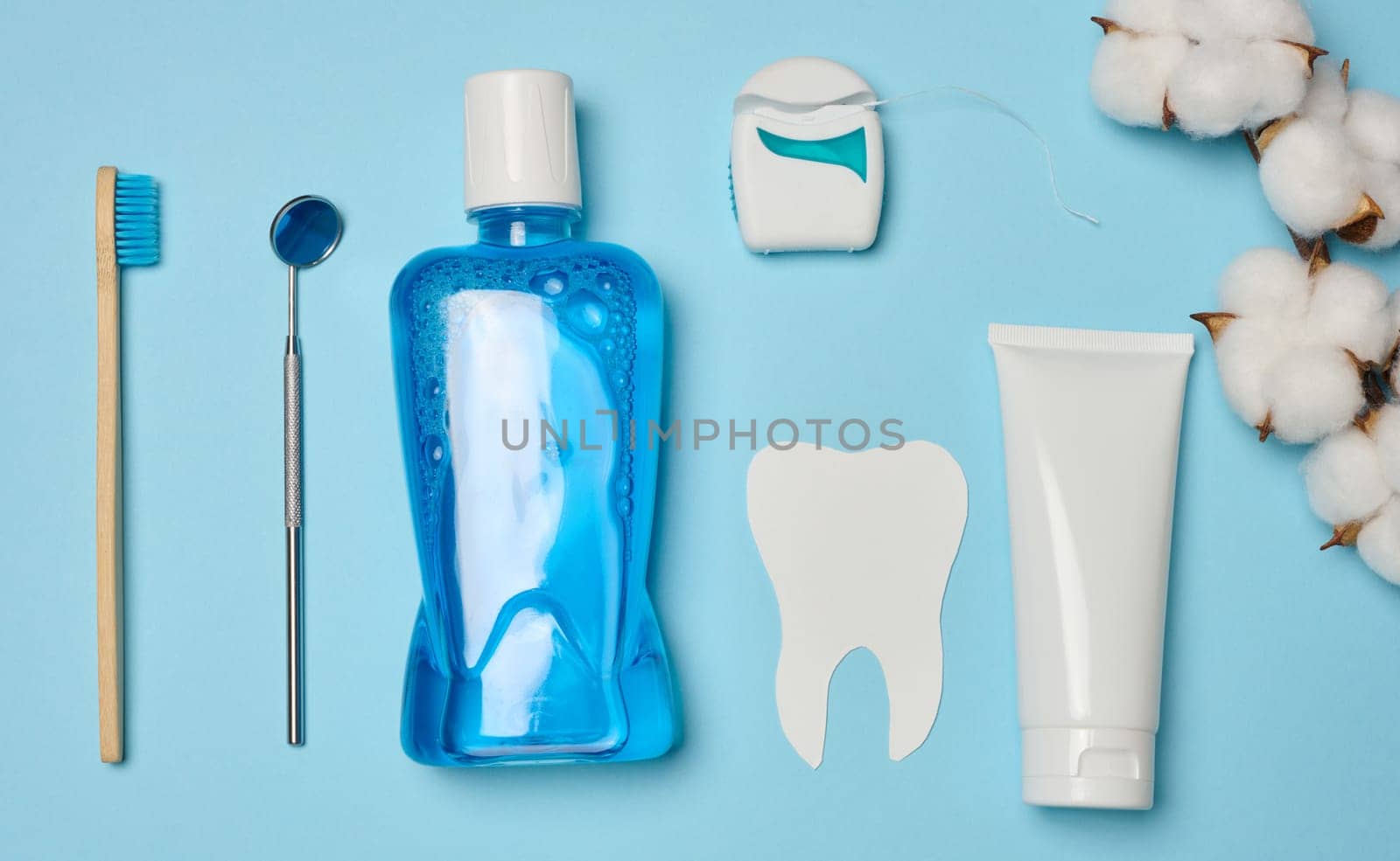 Mouthwash, toothpaste tube, dental floss and medical mirror on a blue background, oral hygiene