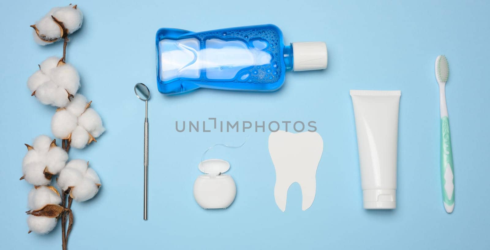 Mouthwash, toothpaste tube, dental floss and medical mirror on a blue background, oral hygiene