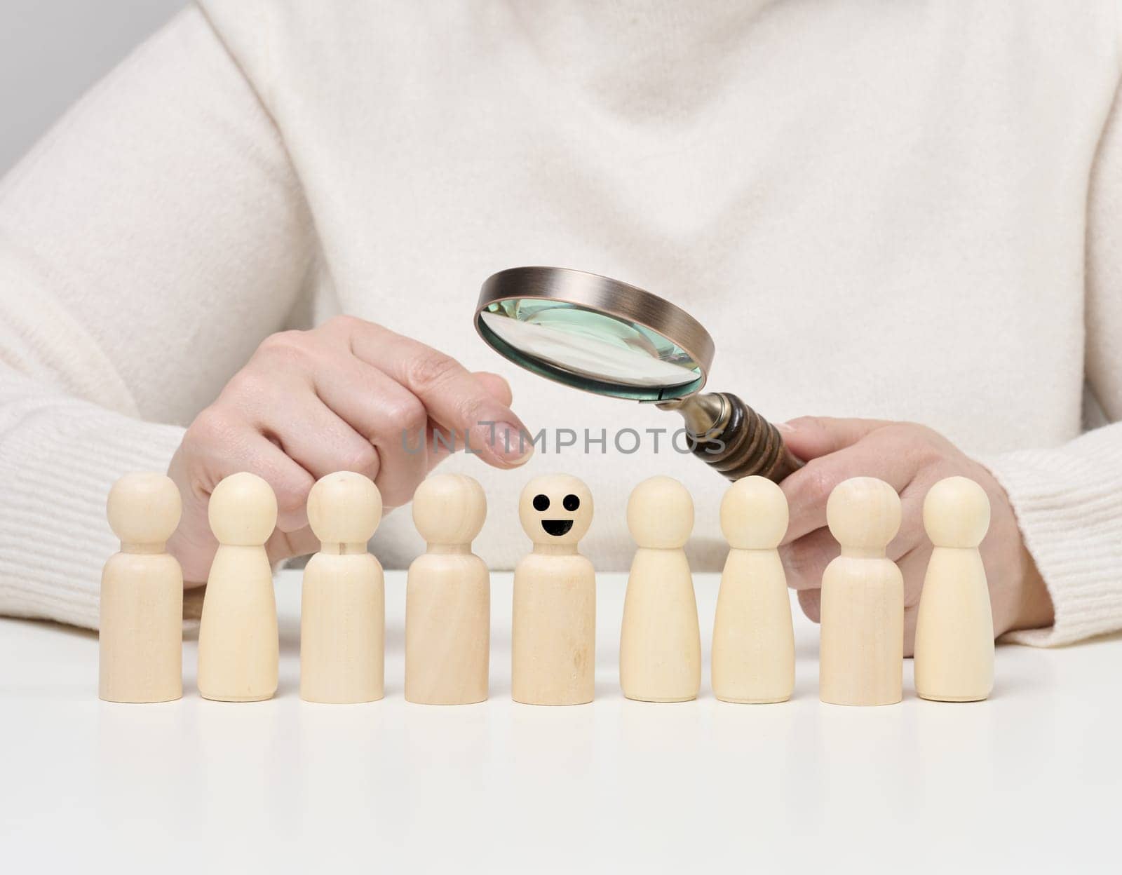Woman holding a magnifying glass and wooden men on a white table. Personnel recruitment concept by ndanko