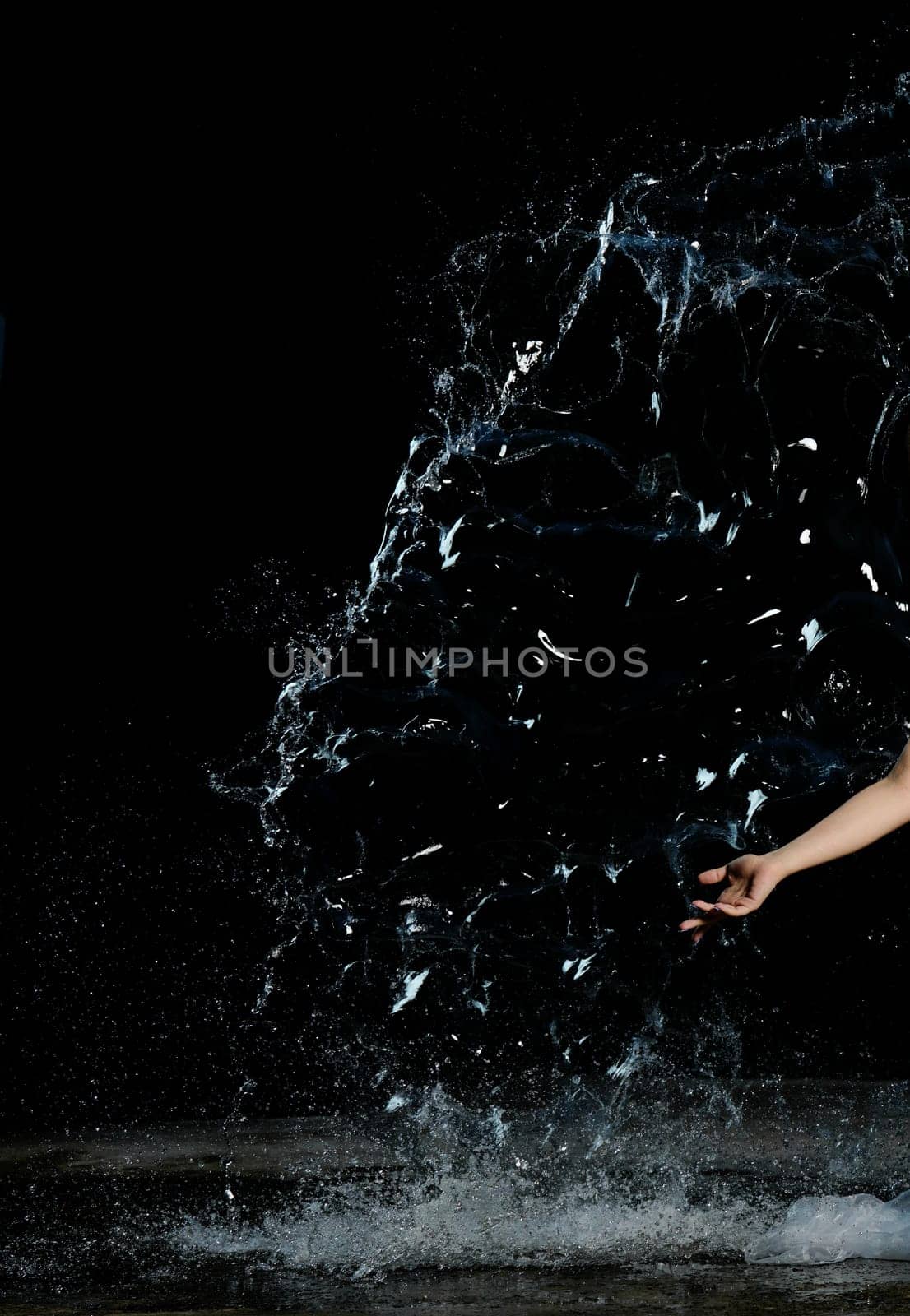 Woman's hand and a splash of clear water with drops on a black background