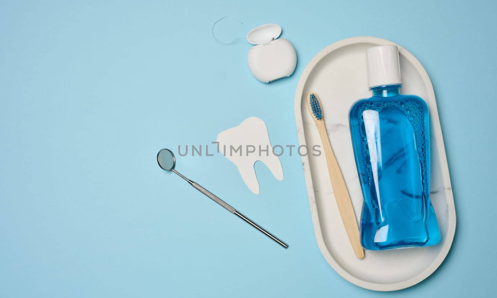 Mouthwash, toothpaste tube, dental floss and medical mirror on a blue background, oral hygiene. Top view