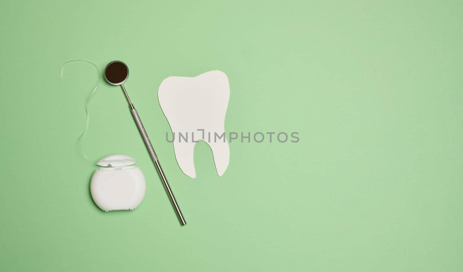 Dental floss and paper teeth on green background, oral hygiene, top view