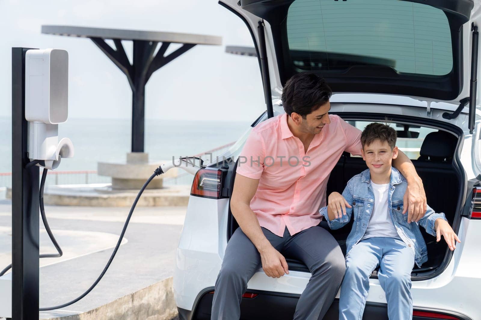 Family road trip vacation traveling by the sea with electric car, father and son recharge EV car with green and clean energy. Natural travel and eco-friendly car for sustainable environment. Perpetual