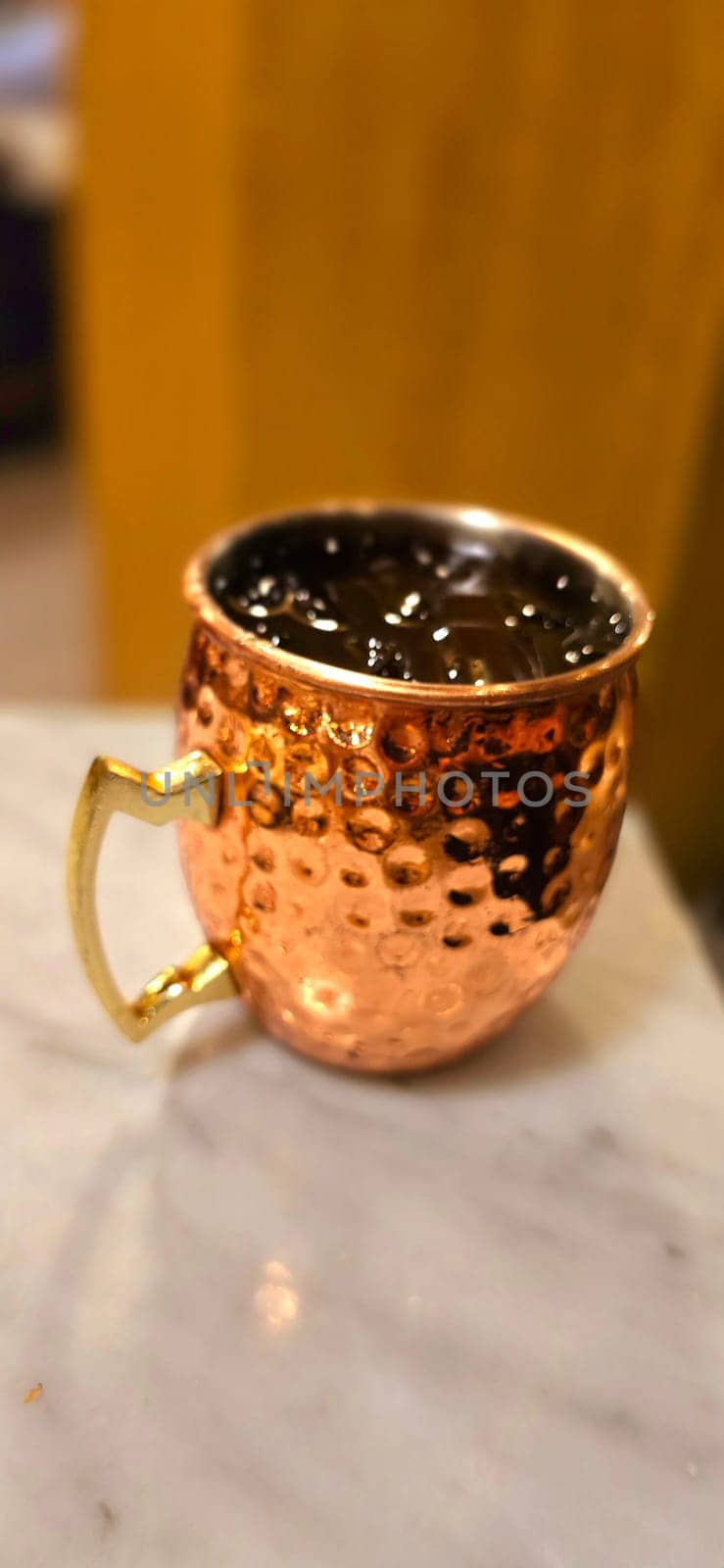 Traditional iced tea served in a unique and artistic brass cup , ice tea garnished with rosemary twigs in a restaurant