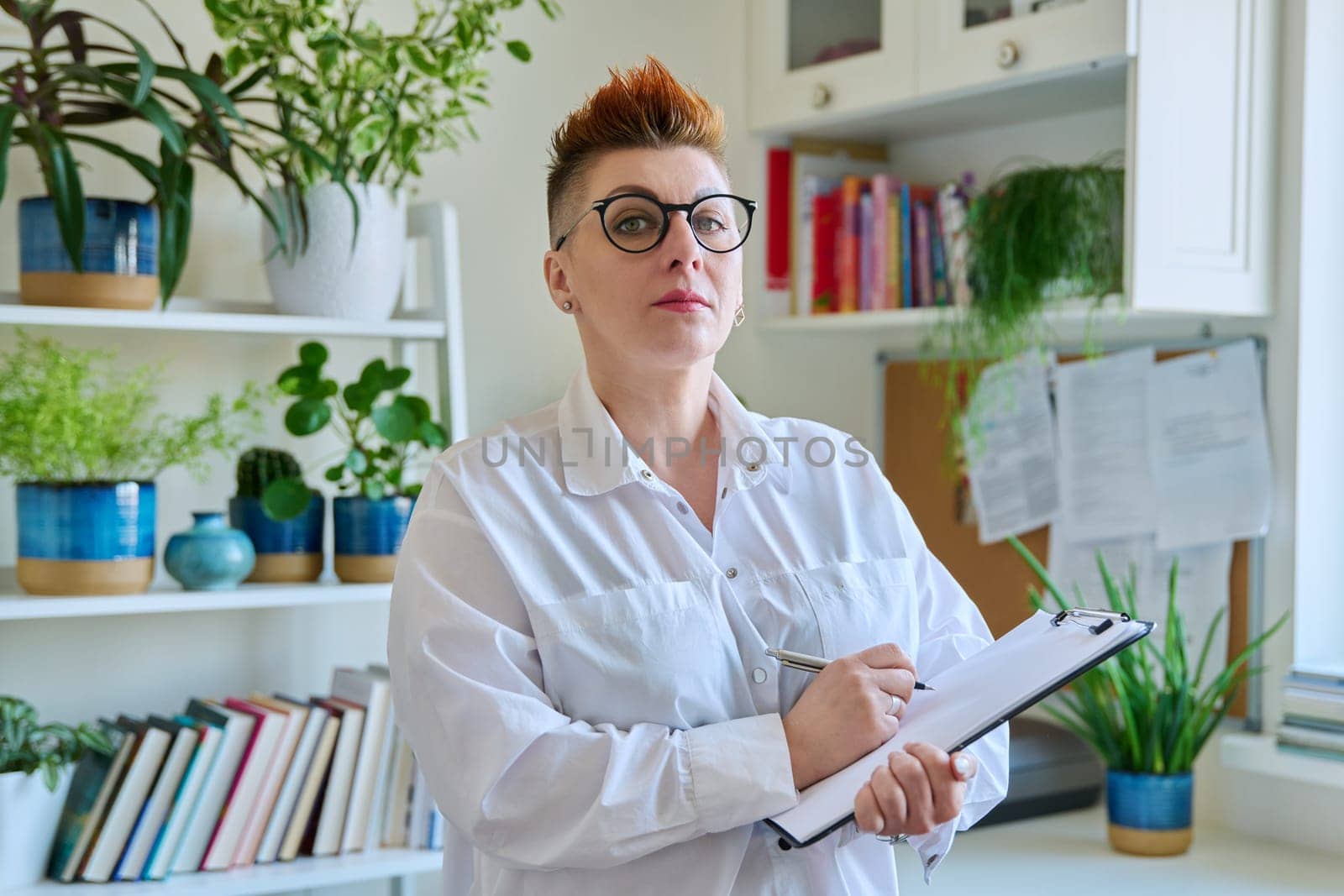 Middle aged confident successful business woman with clipboard at workplace. Remote business, teaching, work concept