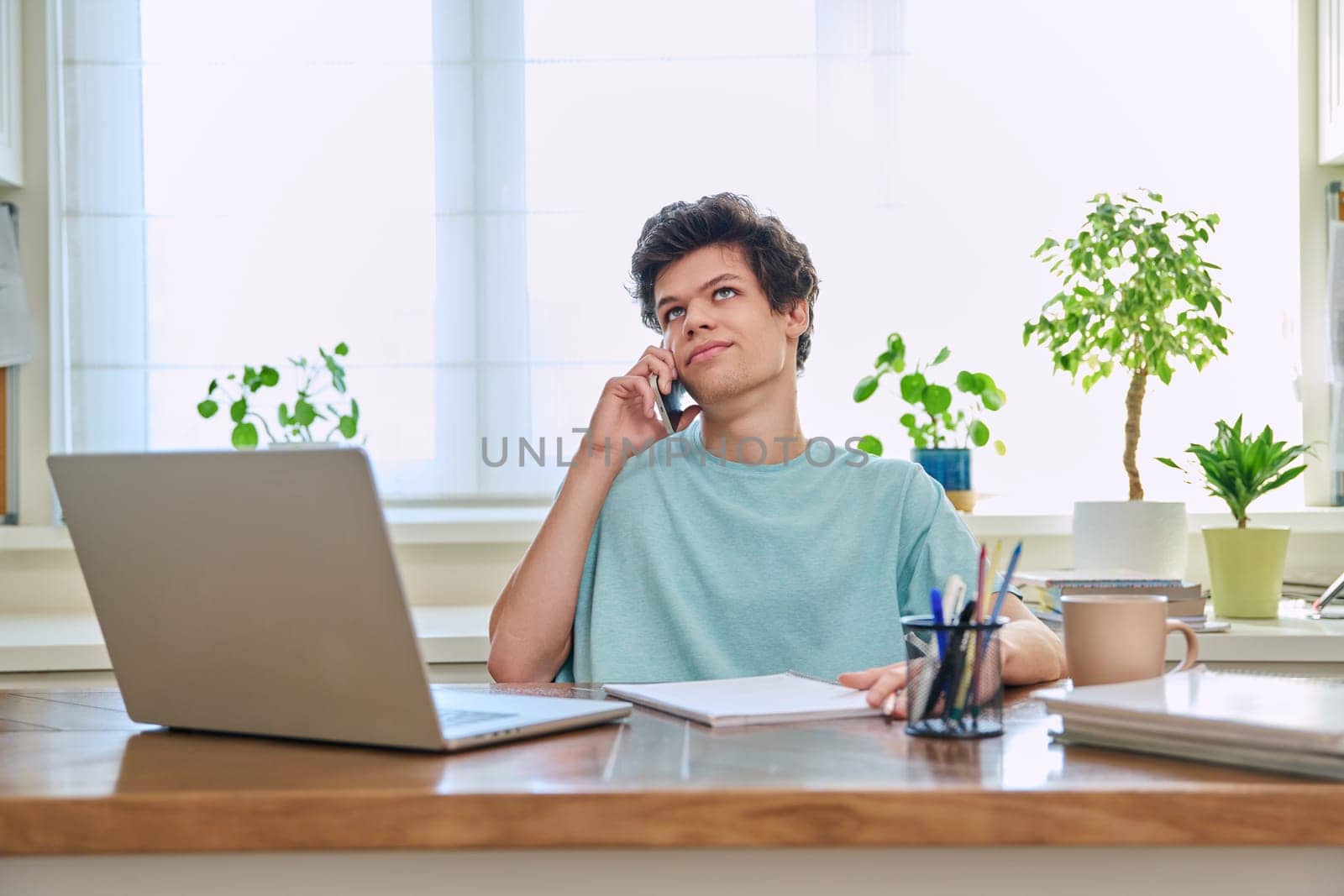 Young guy talking on the phone, sitting at his desk at home.