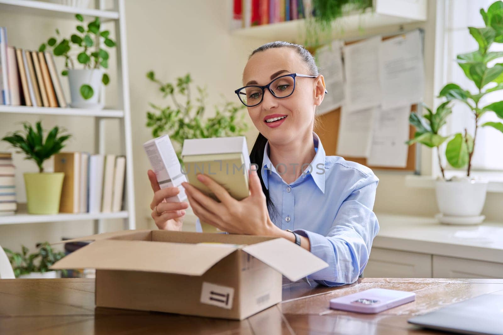 Satisfied female consumer buyer sitting at home unpacking cardboard box with online purchases. Happy woman unpacking boxes with cosmetics care products perfumes. Delivery by mail online store