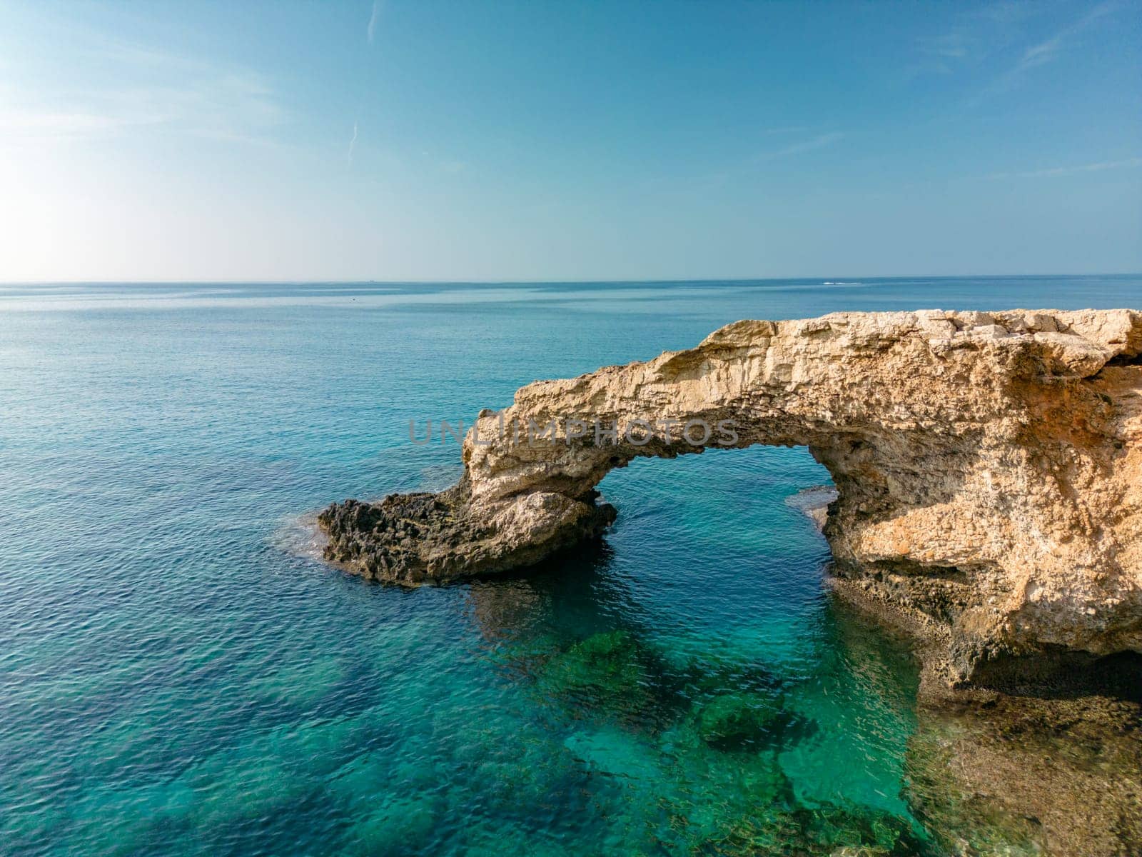 Love bridge near Ayia Napa in Cyprus. Aerial panoramic view of summer rocky landscape in Cavo Greco National park, romantic turquoise sea waves and natural arch of bridge from rocks in water