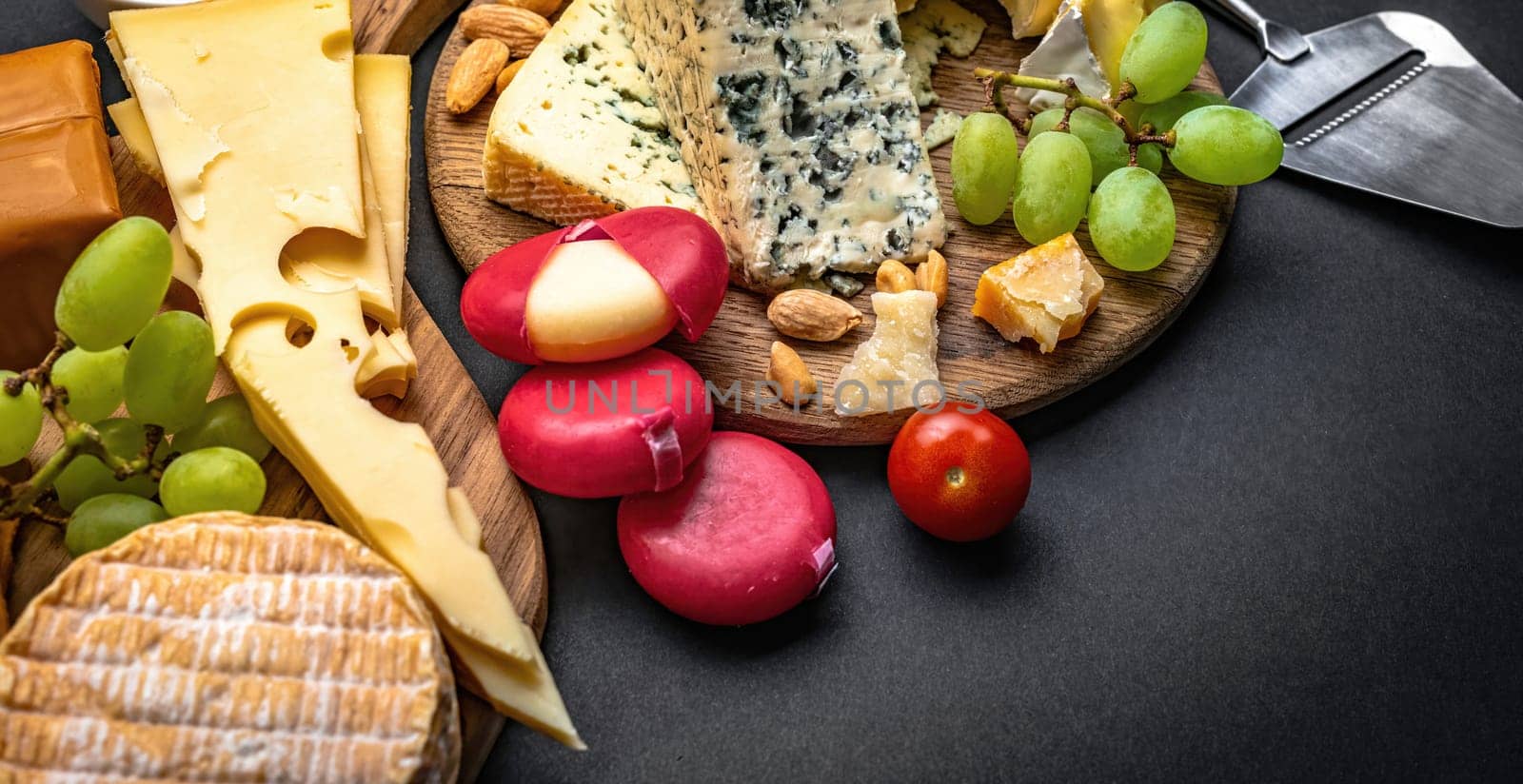 Different kinds of cheese served with grape and tomato for gourmet nutrition. Organic brie and camembert set with nuts delicatessen on black table