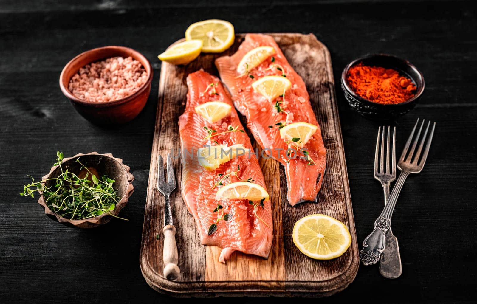 Fresh trout salmon filet with rosemary and lemons on wooden board ready served with spicies, pink salt and hearbs. Omega orange fish with citrus fruit for healthy nutrition