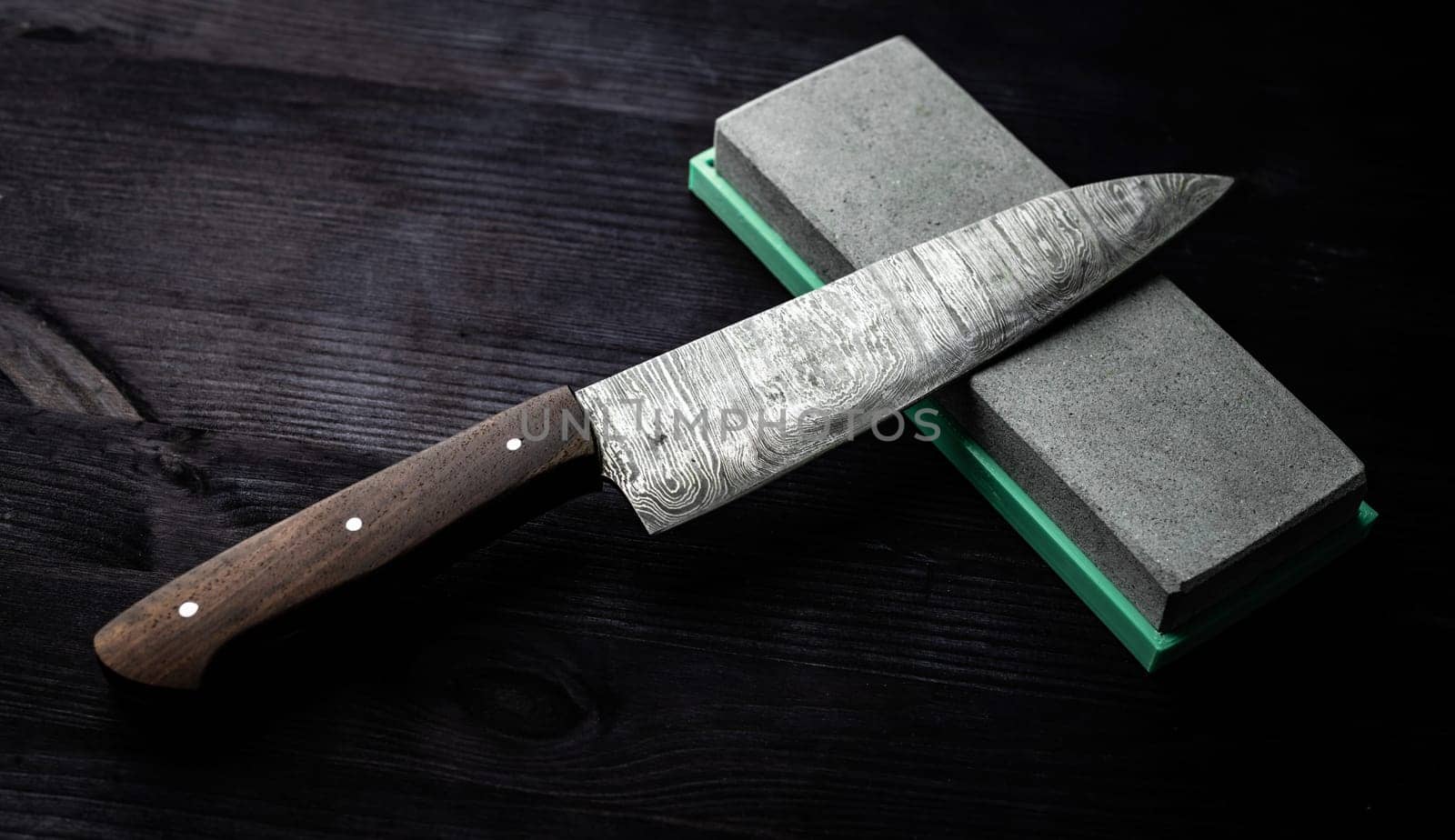 Sharp Chef's Kitchen Knife And Sharpening Stone Lie On Dark Table