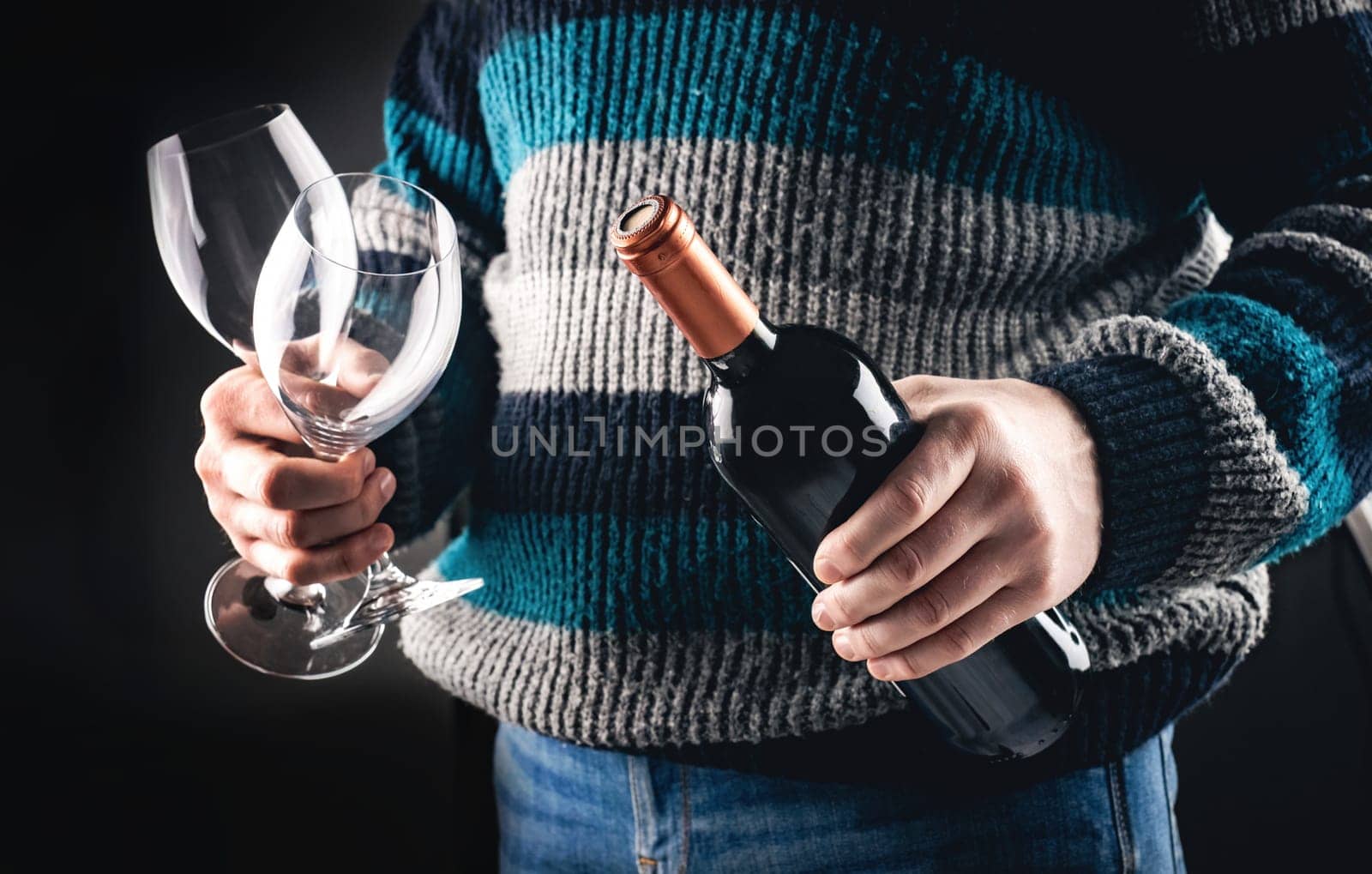 Man holding wine bottle and glasses closeup on black background. Guy with grape alcohol beverage and wineglasses