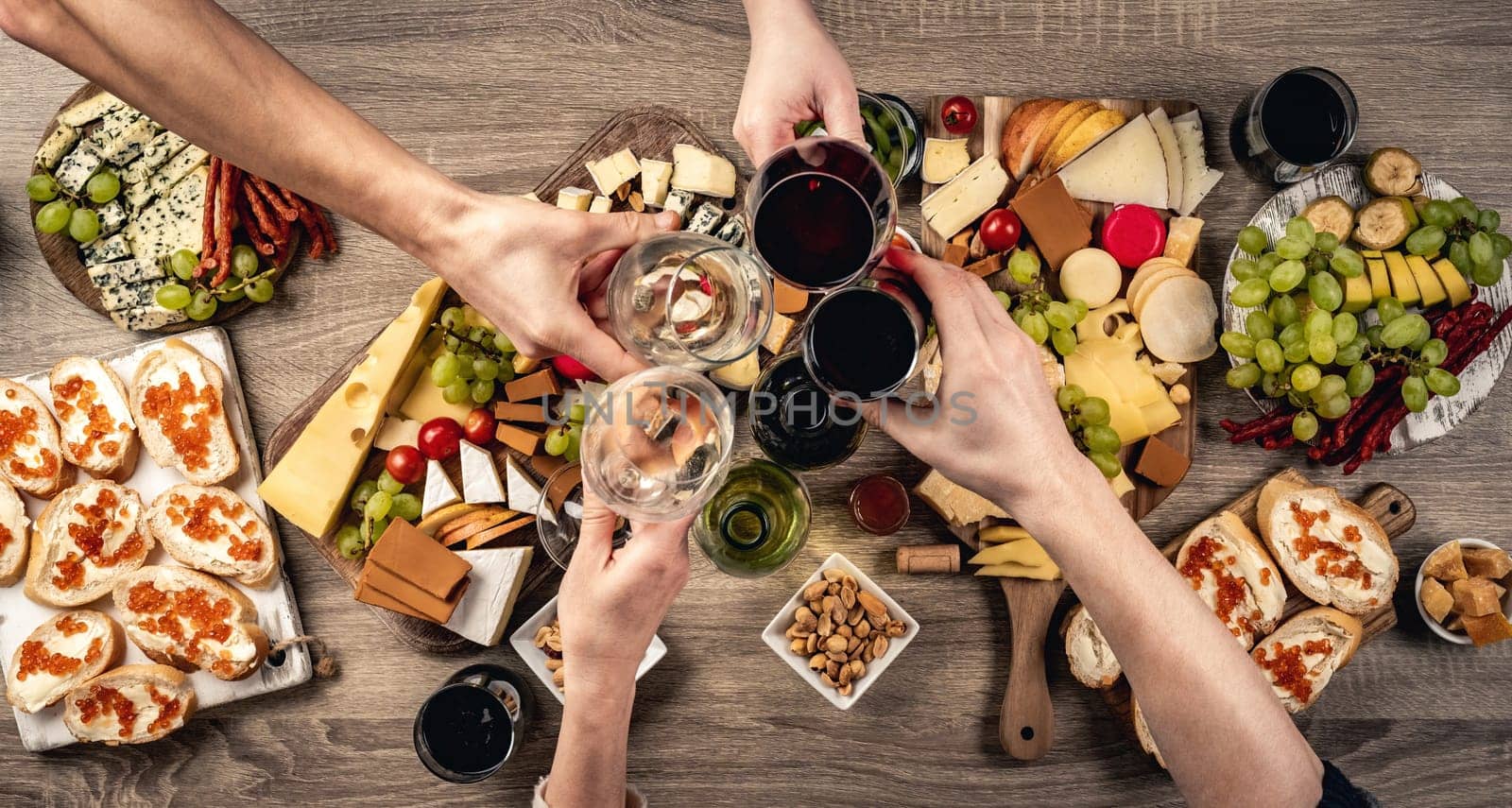 People hands with wine glasses, grape and variety of cheese kinnds. Delicatessen food collection with alcohol beverage