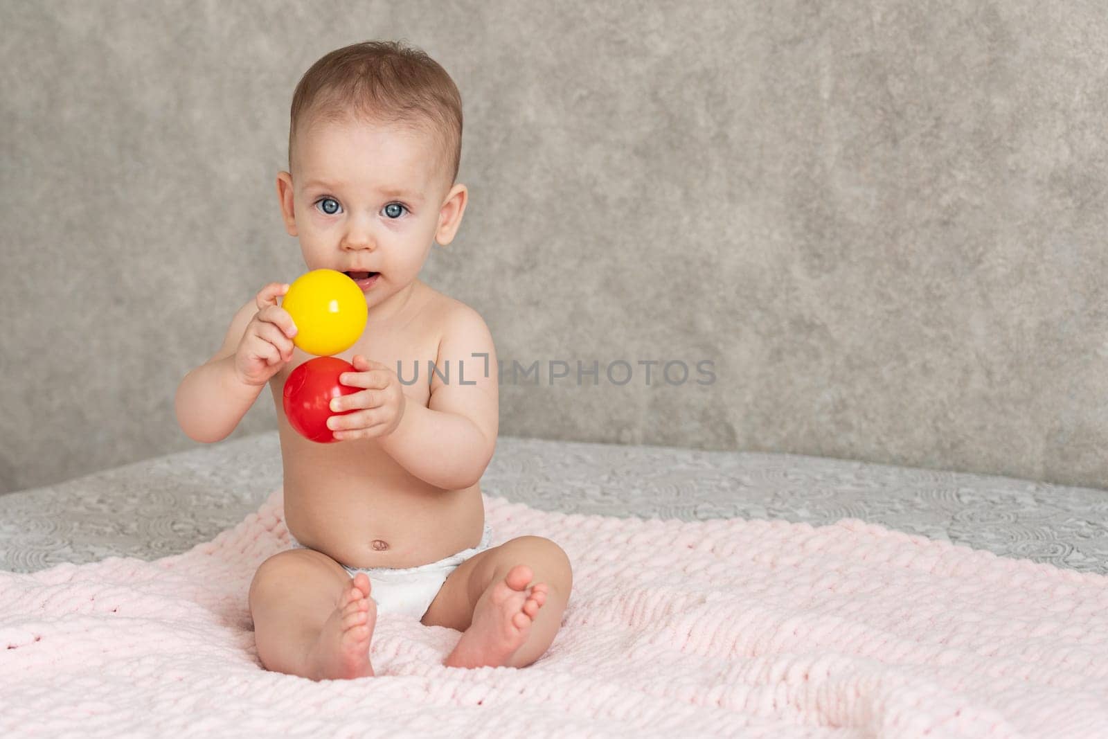 Shy little girl holds colored balls in front of her with which she plays.