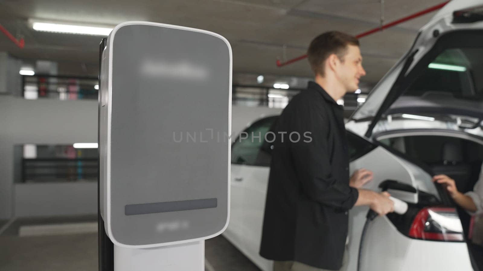 Young couple travel with EV electric car to shopping center parking lot charging in downtown city showing urban sustainability lifestyle by green clean rechargeable energy of electric vehicle innards