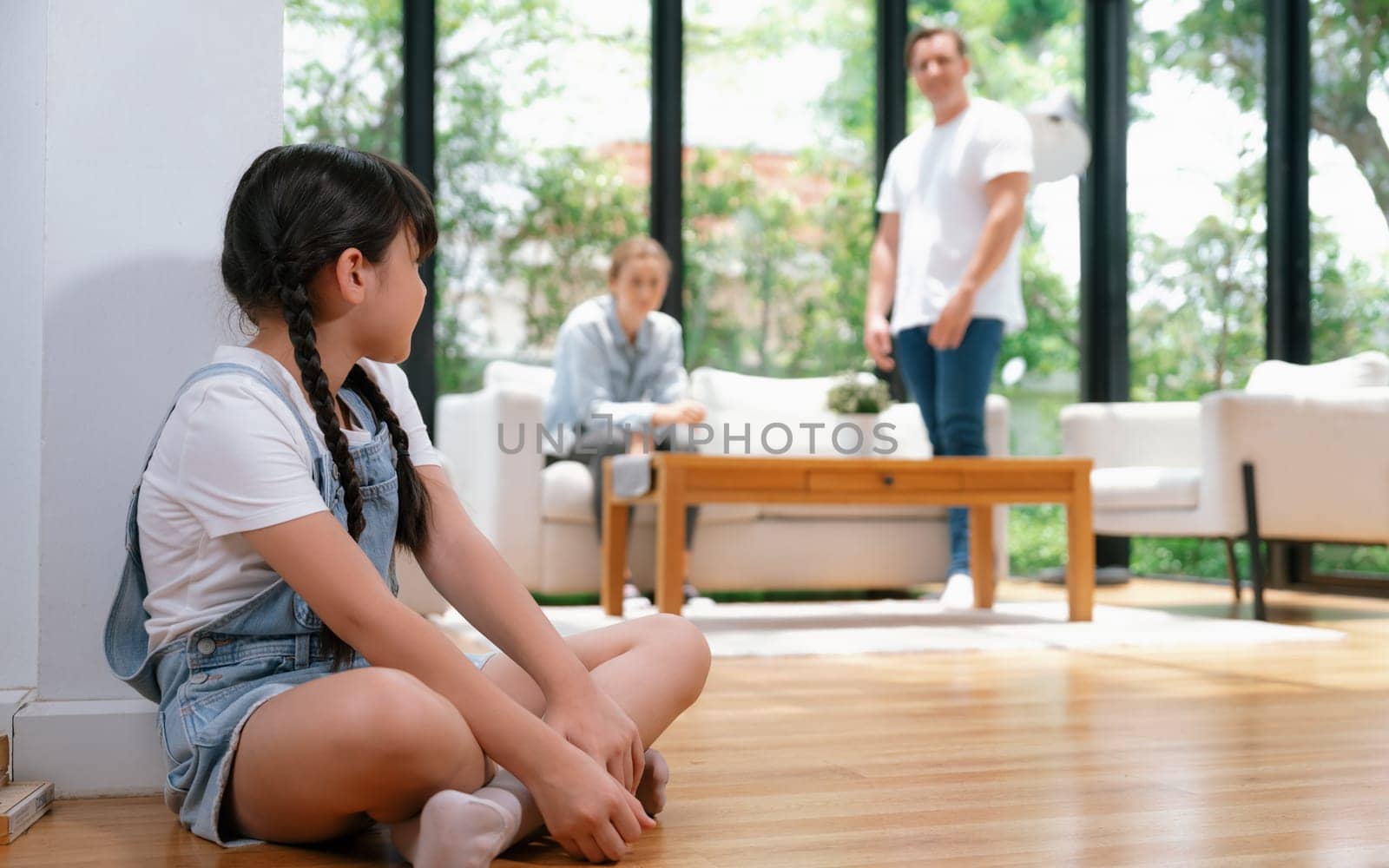 Stressed and unhappy young girl huddle in corner crying and sad while her parent arguing in background. Domestic violence at home and traumatic childhood develop to depression. Synchronos