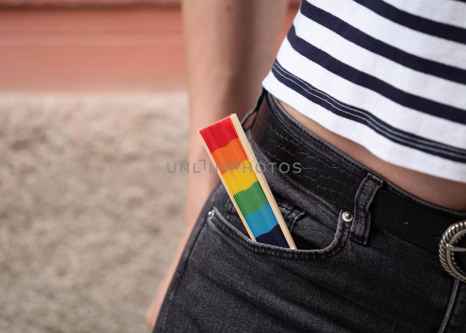 Close up view of a gay person holding a rainbow colored spanish fan in the pocket as a sign to support LGBTQ community.